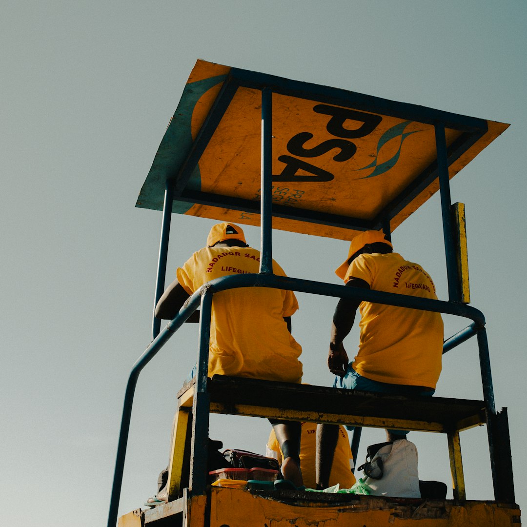 Lifeguards in yellow shirts on a tall chair.